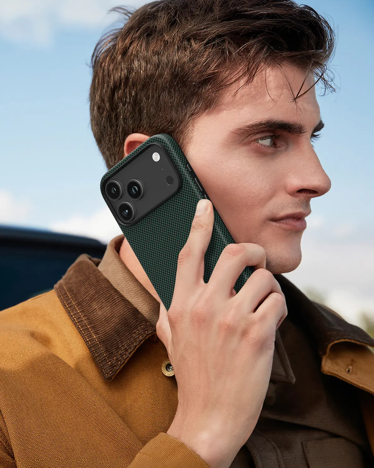 Man making a call with an iPhone 18 Pro Max protected by NOX Pine Green aramid case in modern outdoor setting.