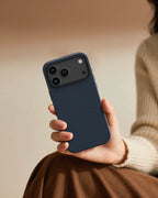 Hand holding an iPhone 18 Pro Max protected by NOX Steel Blue aramid fiber case in warm indoor setting, showing slim and comfortable grip.