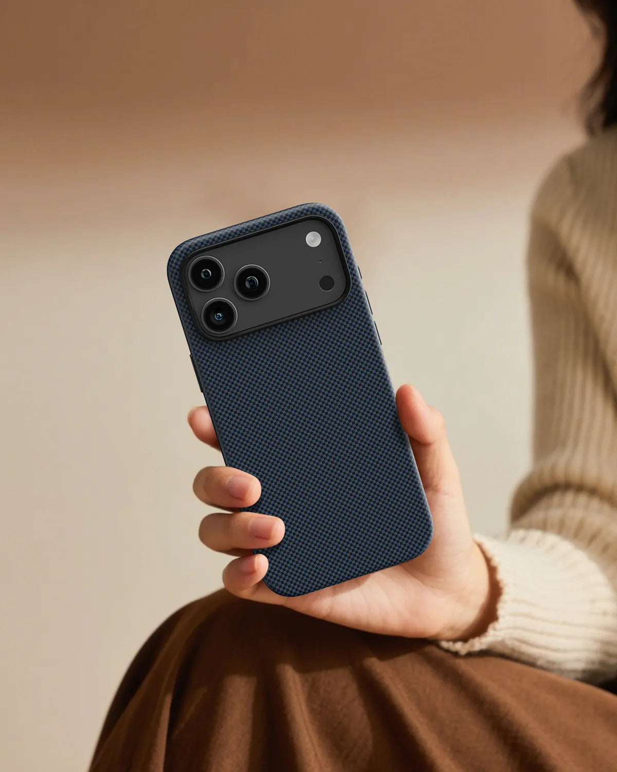 Hand holding an iPhone 18 Pro Max protected by NOX Steel Blue aramid fiber case in warm indoor setting, showing slim and comfortable grip.
