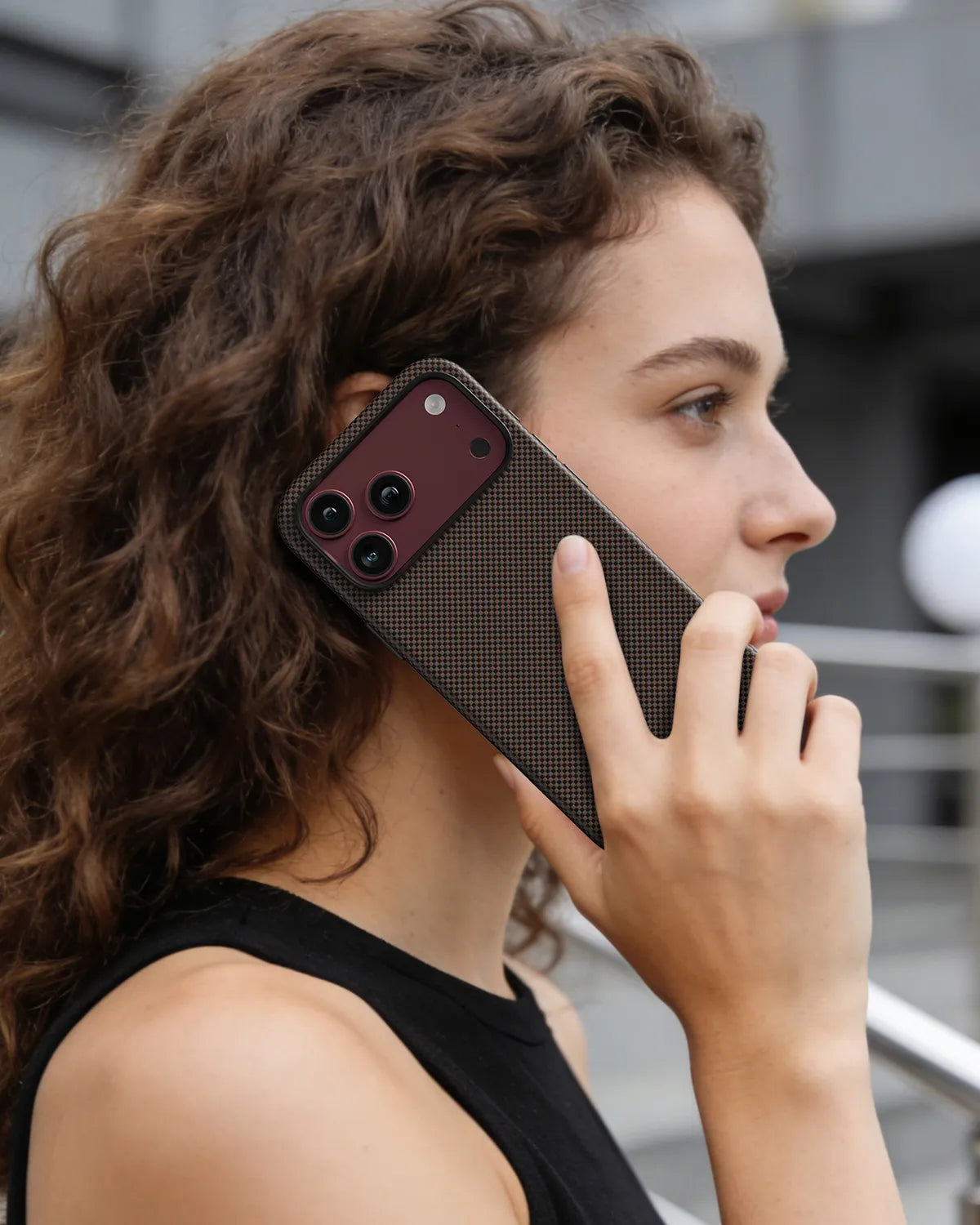 Woman holding an iPhone 18 Pro Max with NOX Sunset Copper aramid fiber case, showing sleek tactile grip and executive style.